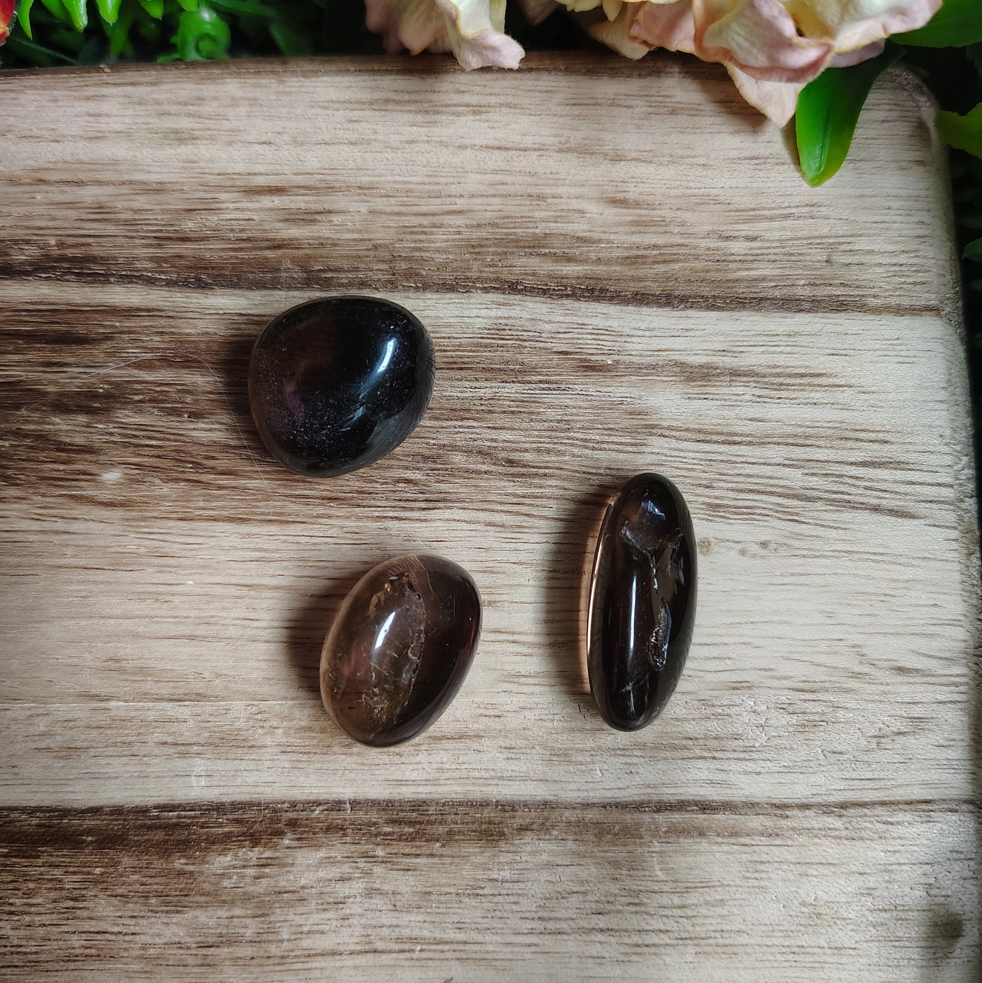Three dark stones on a wooden surface with flowers in the corner