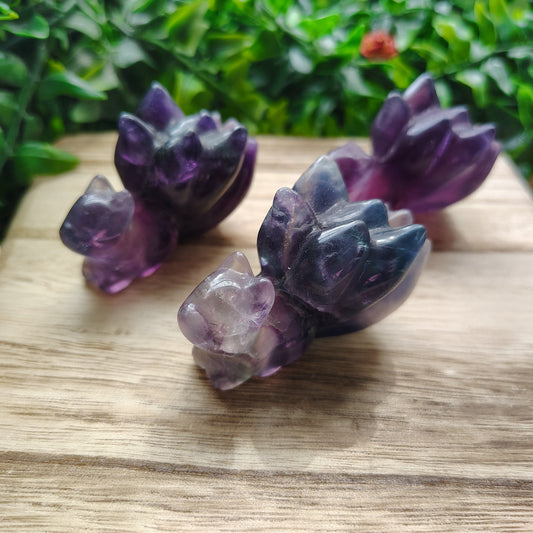 Three purple crystal animal figurines on a wooden surface with greenery in the background