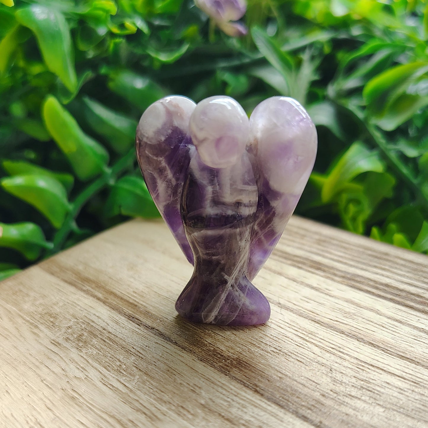 Amethyst crystal on a wooden surface with greenery and flowers in the background