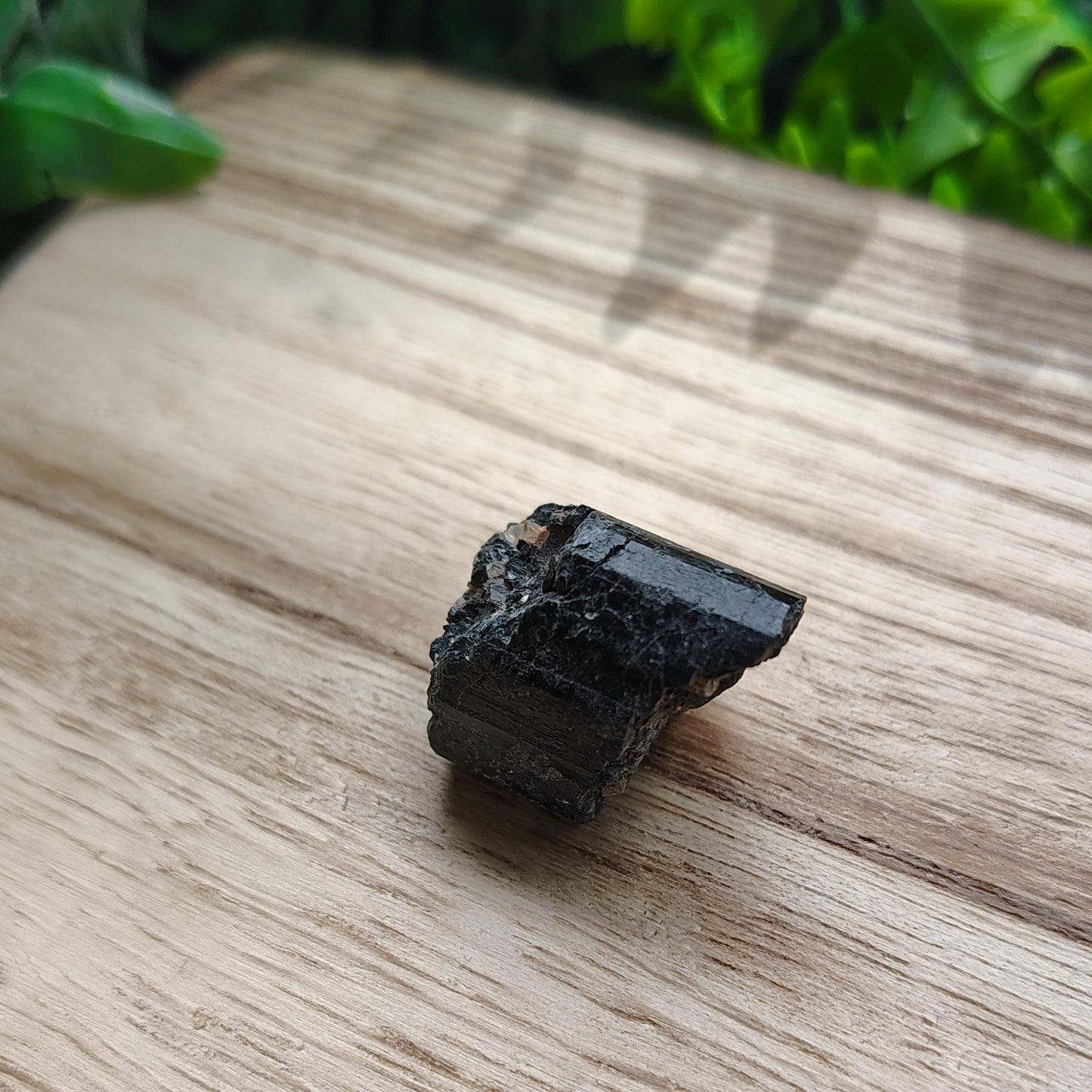 Black crystal on a wooden surface with green leaves in the background
